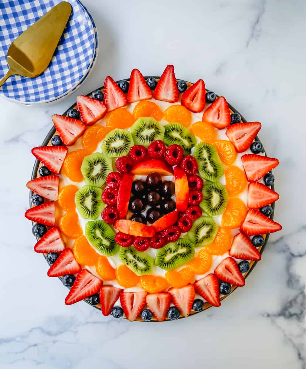 Fruit Pizza with a Sugar Cookie Crust is made with a large, pizza-sized baked sugar cookie and topped with a sweet cream cheese whipped cream and sprinkled with glazed fresh fruit. 