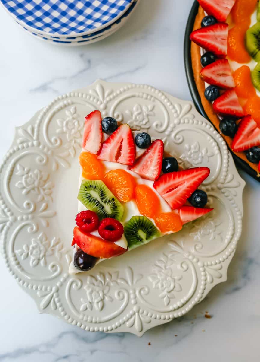 Fruit Pizza with a Sugar Cookie Crust is made with a large, pizza-sized baked sugar cookie and topped with a sweet cream cheese whipped cream and sprinkled with glazed fresh fruit. 