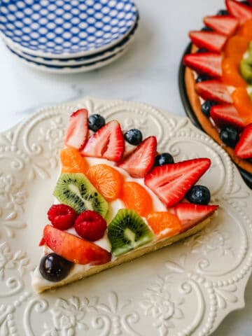 Fruit Pizza with a Sugar Cookie Crust is made with a large, pizza-sized baked sugar cookie and topped with a sweet cream cheese whipped cream and sprinkled with glazed fresh fruit. 