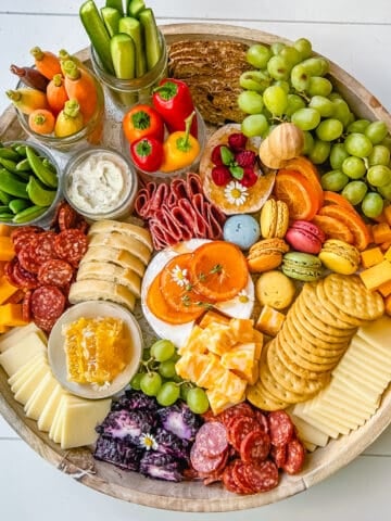 A beautiful Spring Charcuterie Board with fresh ripe fruits, creamy cheeses, crisp vegetables, cured meats, crackers, French baguette slices, honeycomb, macarons, and edible flowers. This is a perfect Spring entertaining board.