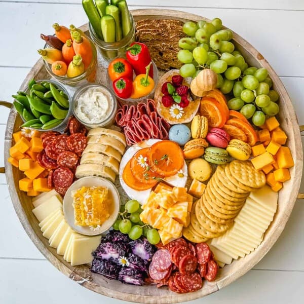 A beautiful Spring Charcuterie Board with fresh ripe fruits, creamy cheeses, crisp vegetables, cured meats, crackers, French baguette slices, honeycomb, macarons, and edible flowers. This is a perfect Spring entertaining board.