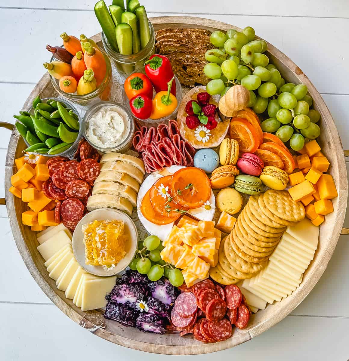 A beautiful Spring Charcuterie Board with fresh ripe fruits, creamy cheeses, crisp vegetables, cured meats, crackers, French baguette slices, honeycomb, macarons, and edible flowers. This is a perfect Spring entertaining board.