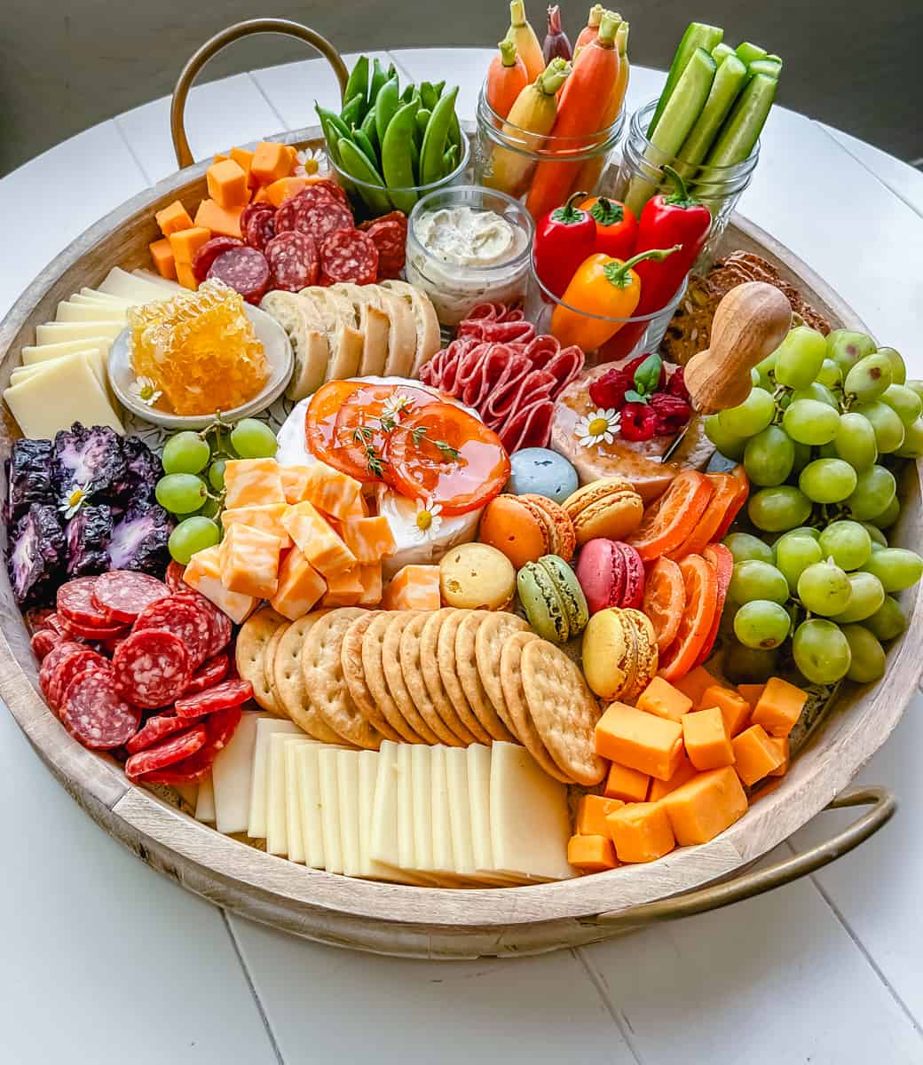 A beautiful Spring Charcuterie Board with fresh ripe fruits, creamy cheeses, crisp vegetables, cured meats, crackers, French baguette slices, honeycomb, macarons, and edible flowers. This is a perfect Spring entertaining board.