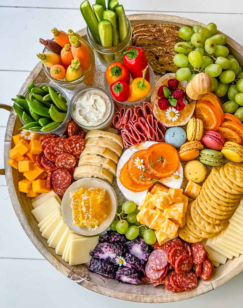 A beautiful Spring Charcuterie Board with fresh ripe fruits, creamy cheeses, crisp vegetables, cured meats, crackers, French baguette slices, honeycomb, macarons, and edible flowers. This is a perfect Spring entertaining board.