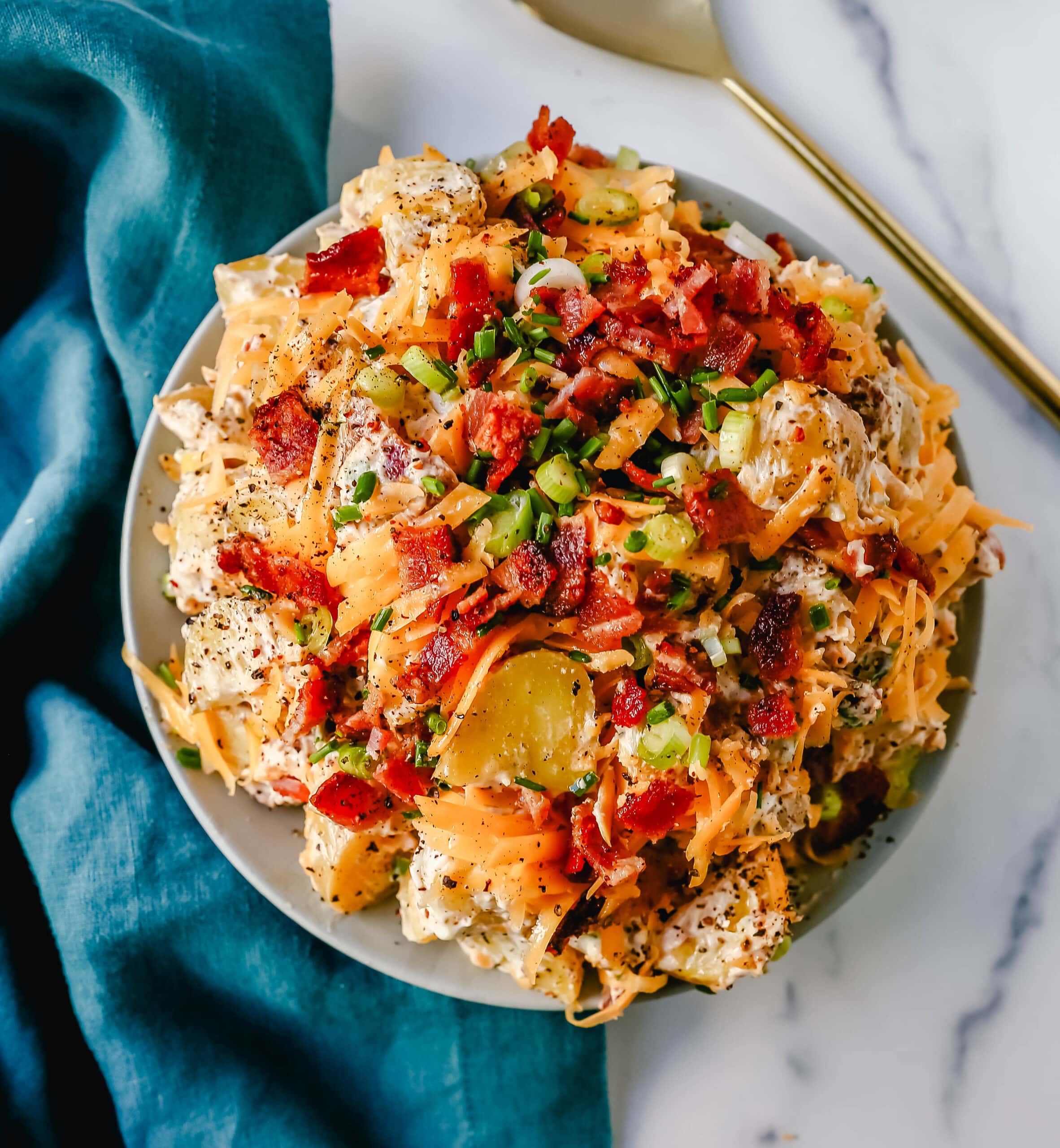 The Best Loaded Potato Salad Recipe is made with creamy gold potatoes, crispy bacon, cheddar cheese, green onions, sour cream, mayonnaise, seasoned salt, and pepper. The perfect baked potato salad recipe is perfect for your next party, potluck, or as a BBQ side dish.