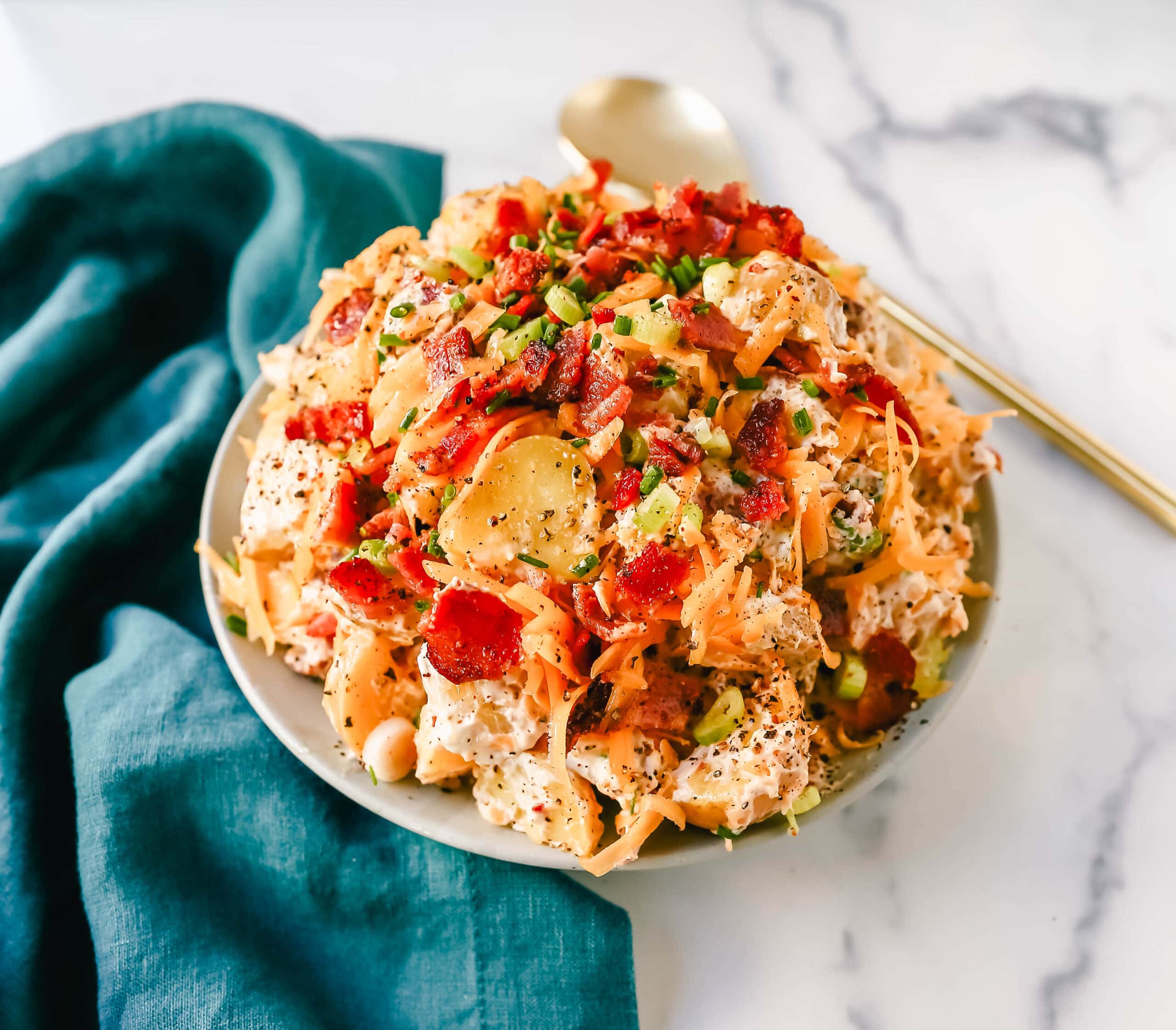 The Best Loaded Potato Salad Recipe is made with creamy gold potatoes, crispy bacon, cheddar cheese, green onions, sour cream, mayonnaise, seasoned salt, and pepper. The perfect baked potato salad recipe is perfect for your next party, potluck, or as a BBQ side dish.