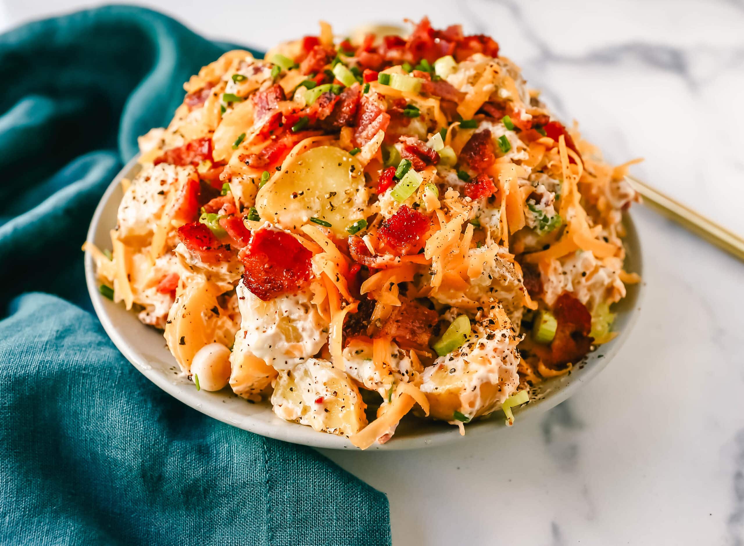 The Best Loaded Potato Salad Recipe is made with creamy gold potatoes, crispy bacon, cheddar cheese, green onions, sour cream, mayonnaise, seasoned salt, and pepper. The perfect baked potato salad recipe is perfect for your next party, potluck, or as a BBQ side dish.