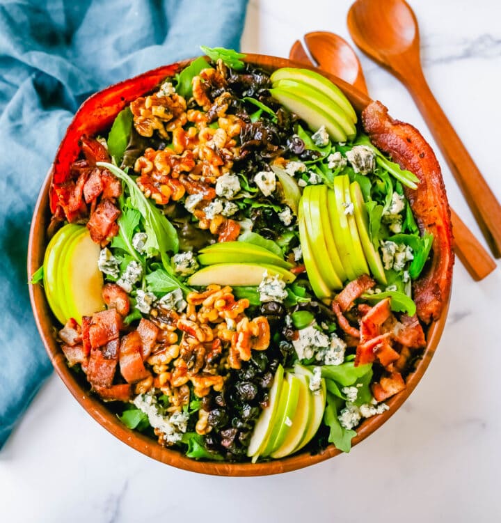 Fall Harvest Salad made with fresh apples, candied walnuts, dried cranberries, feta or blue cheese, crispy bacon all tossed with arugula or spring mix in a homemade apple cider vinegar dressing. The best Fall salad recipe!