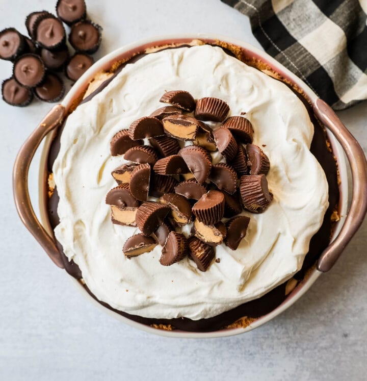 No-Bake Chocolate Peanut Butter Pie with a graham cracker crust, creamy peanut butter filling with peanut butter cups, chocolate ganache, and topped with fresh whipped cream and peanut butter cups. The best chocolate peanut butter pie recipe!