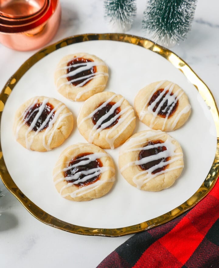 Raspberry Almond Jam Thumbprint Cookies are buttery shortbread cookies made with only butter, sugar, flour, and almond extract, topped with jam, and baked until soft and topped with homemade vanilla or almond glaze. A festive and delicious Christmas cookie recipe!