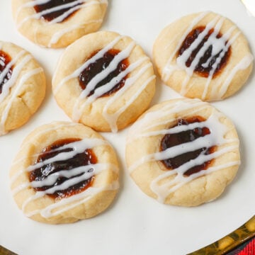 Raspberry Almond Jam Thumbprint Cookies are buttery shortbread cookies made with only butter, sugar, flour, and almond extract, topped with jam, and baked until soft and topped with homemade vanilla or almond glaze. A festive and delicious Christmas cookie recipe!