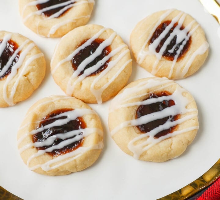 Raspberry Almond Jam Thumbprint Cookies are buttery shortbread cookies made with only butter, sugar, flour, and almond extract, topped with jam, and baked until soft and topped with homemade vanilla or almond glaze. A festive and delicious Christmas cookie recipe!