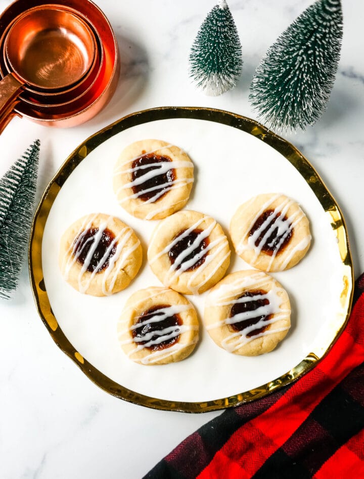 Raspberry Almond Jam Thumbprint Cookies are buttery shortbread cookies made with only butter, sugar, flour, and almond extract, topped with jam, and baked until soft and topped with homemade vanilla or almond glaze. A festive and delicious Christmas cookie recipe!