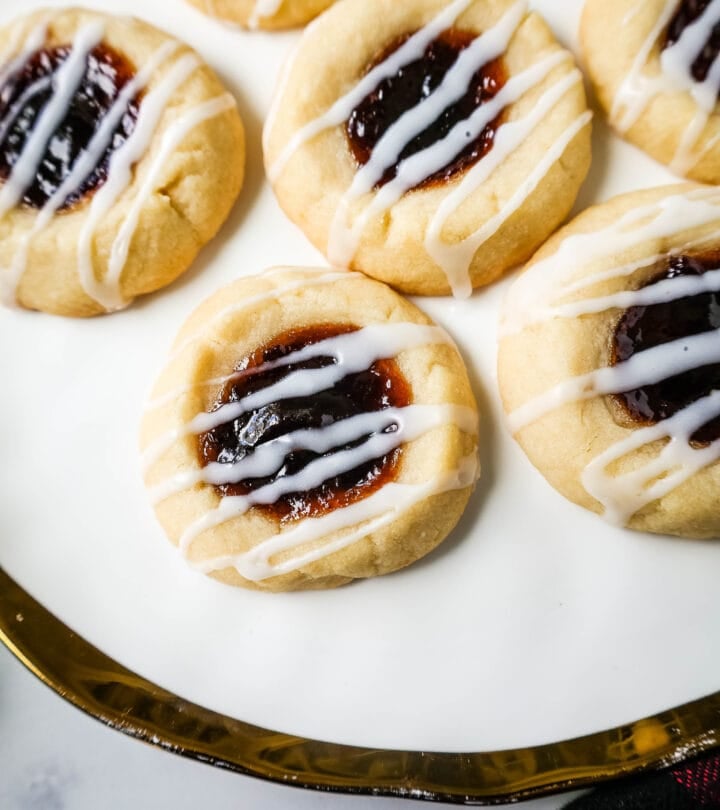 Raspberry Almond Jam Thumbprint Cookies are buttery shortbread cookies made with only butter, sugar, flour, and almond extract, topped with jam, and baked until soft and topped with homemade vanilla or almond glaze. A festive and delicious Christmas cookie recipe!