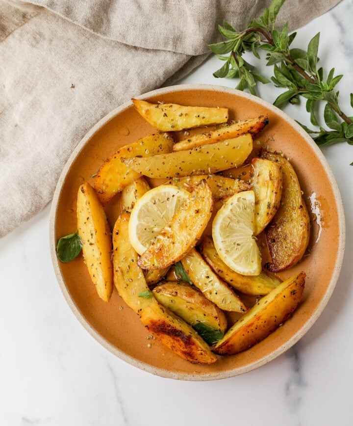 These Greek Roasted Potatoes are infused with extra-virgin olive oil, lemon juice, garlic, oregano, spices, and chicken broth which makes the creamiest roasted potatoes full of Greek flavor.