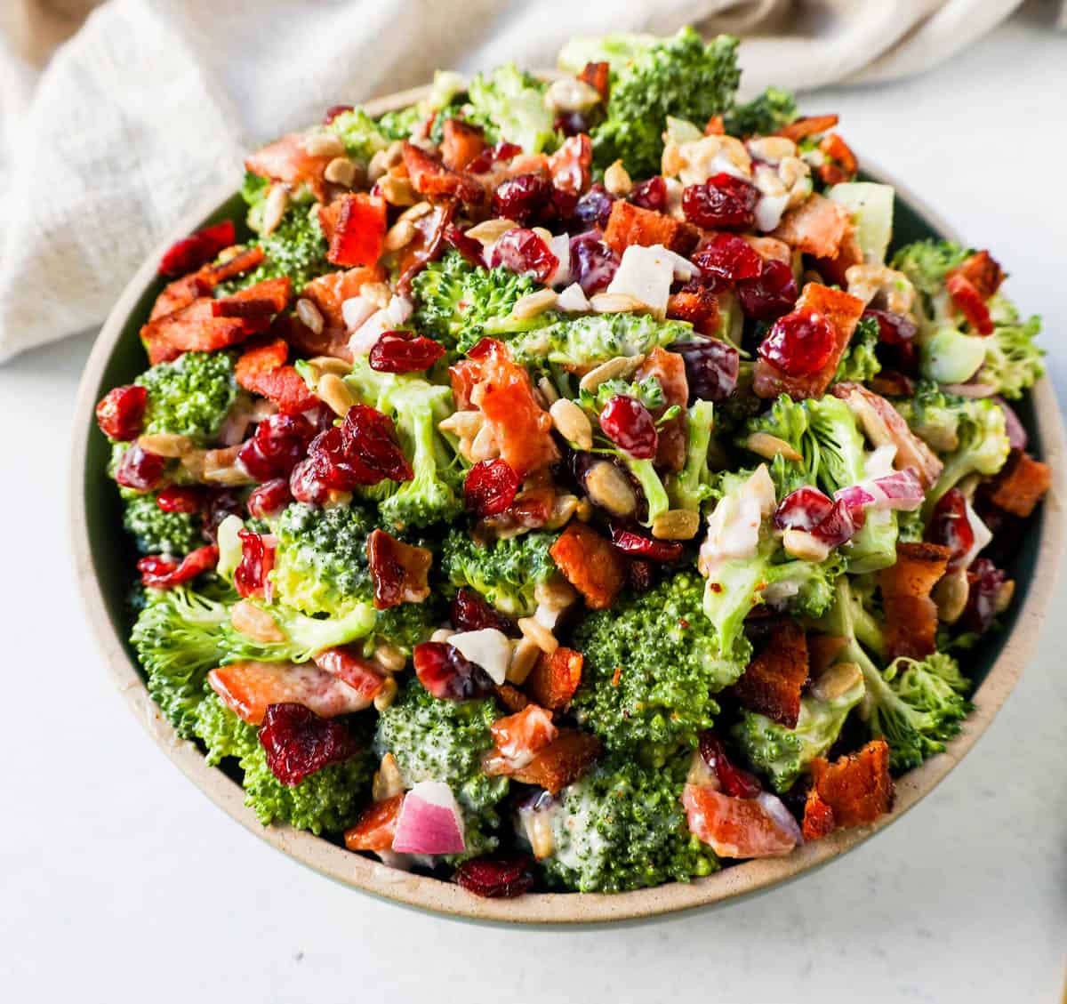 A bowl of homemade broccoli salad. Crunchy, easy broccoli salad with crispy bacon, sweet dried cranberries, onion, and nuts all tossed in a sweet and tangy dressing. Tips for making the best broccoli salad. A classic potluck, BBQ, or summer side dish recipe!
