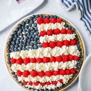 This flag sugar cookie fruit pizza is a festive, delicious, and beautiful patriotic 4th of July dessert featuring a homemade soft sugar cookie crust with a sweet vanilla cream cheese frosting topped with fresh raspberries, blueberries, and homemade whipped cream.