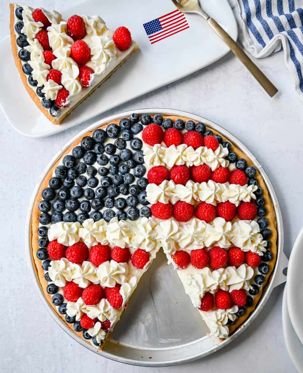 This flag sugar cookie fruit pizza is a festive, delicious, and beautiful patriotic 4th of July dessert featuring a homemade soft sugar cookie crust with a sweet vanilla cream cheese frosting topped with fresh raspberries, blueberries, and homemade whipped cream. 