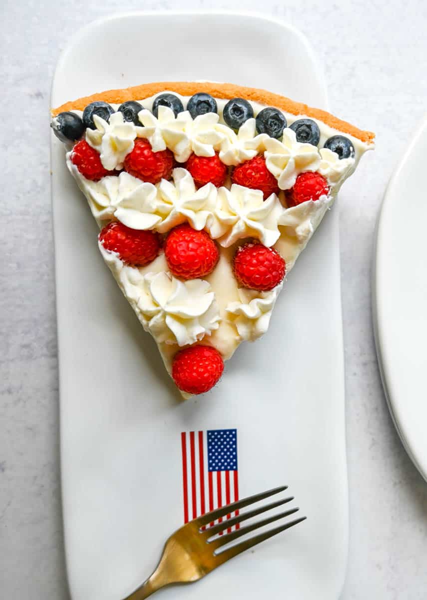 This flag sugar cookie fruit pizza is a festive, delicious, and beautiful patriotic 4th of July dessert featuring a homemade soft sugar cookie crust with a sweet vanilla cream cheese frosting topped with fresh raspberries, blueberries, and homemade whipped cream. 