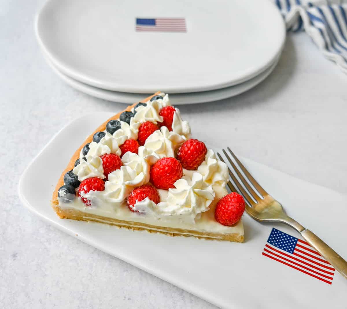 This flag sugar cookie fruit pizza is a festive, delicious, and beautiful patriotic 4th of July dessert featuring a homemade soft sugar cookie crust with a sweet vanilla cream cheese frosting topped with fresh raspberries, blueberries, and homemade whipped cream. 