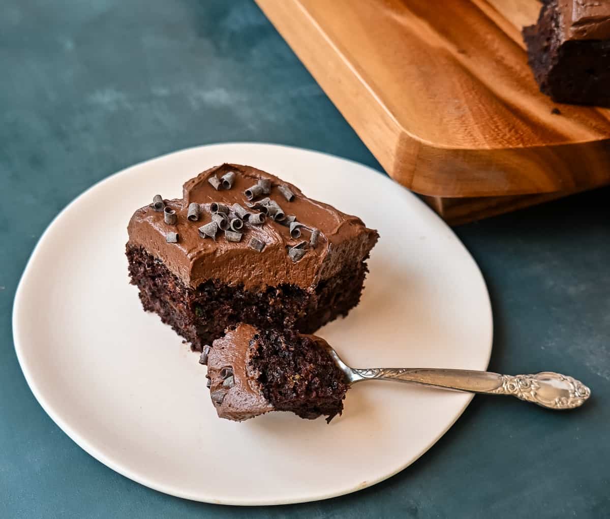 How to make the best chocolate zucchini cake with chocolate frosting. This frosted chocolate zucchini cake is the most moist, rich chocolate cake with the most decadent chocolate frosting. You will not even realize you are eating zucchini! Slice of chocolate zucchini  cake.