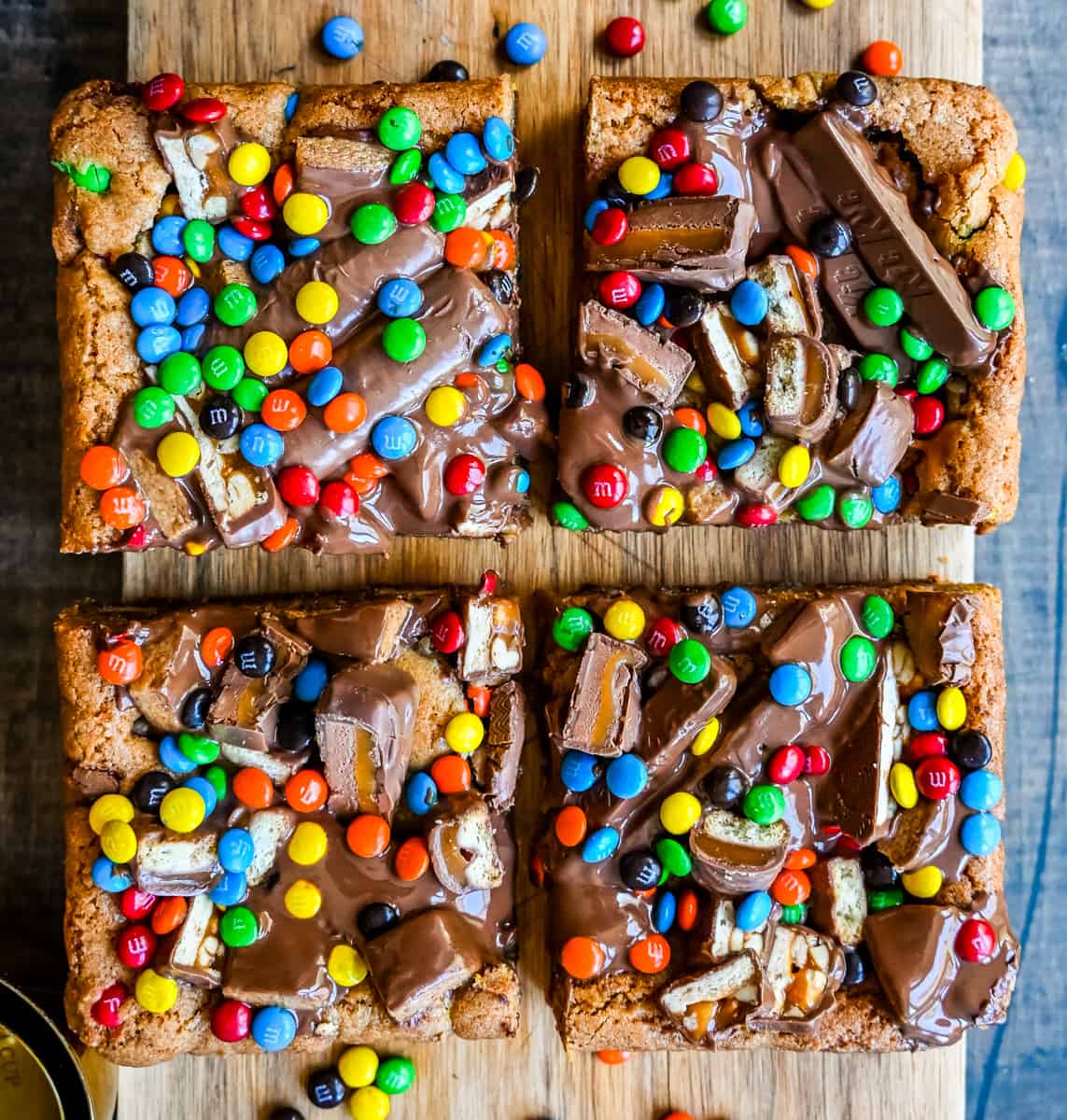 An ooey gooey cookie bar topped with an assortment of candy bars. The perfect candy bar blondie dessert to make with Halloween candy. 