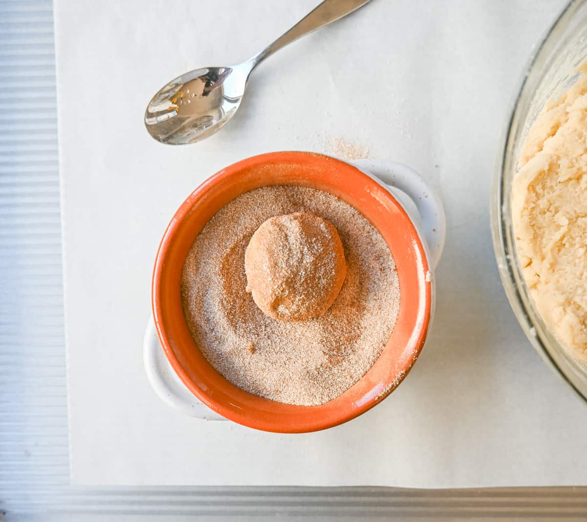 Snickerdoodle cookie dough rolling into cinnamon sugar mixture