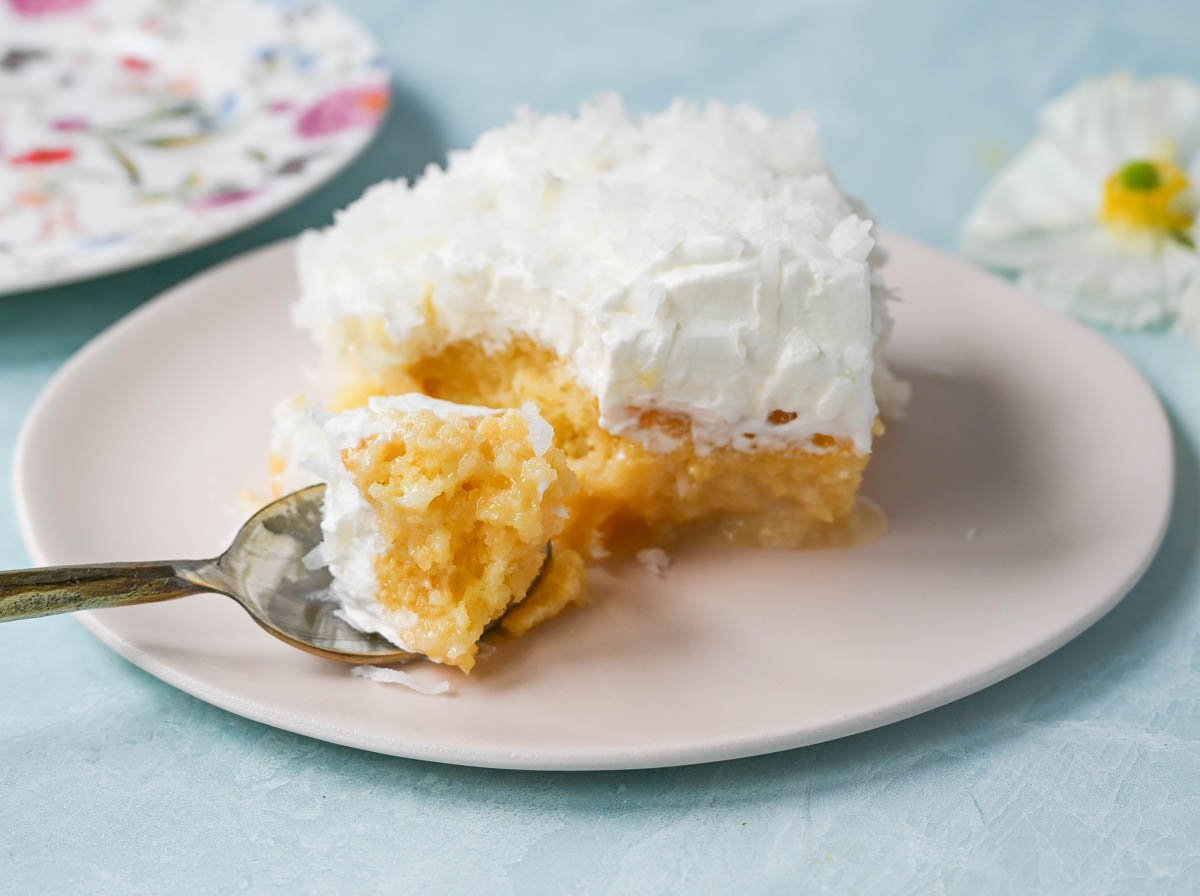 This Coconut Poke Cake is made with a baked cake mix and filled with cream of coconut and sweetened condensed milk and topped with sweet whipped cream and coconut. This Coconut Tres Leches Cake is so easy to make and is perfect for potlucks and parties.