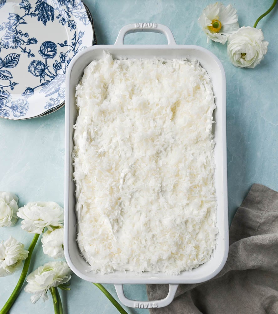 This Coconut Poke Cake is made with a baked cake mix and filled with cream of coconut and sweetened condensed milk and topped with sweet whipped cream and coconut. This Coconut Tres Leches Cake is so easy to make and is perfect for potlucks and parties.