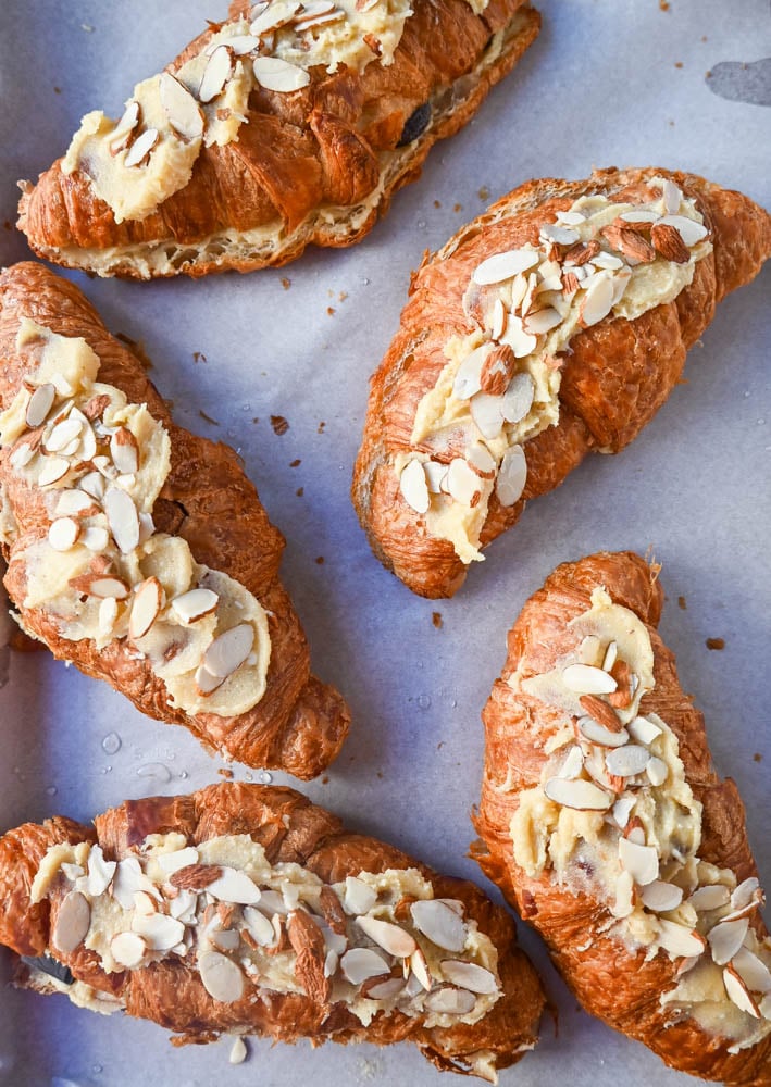 Spreading almond filling and almonds on top of chocolate almond croissants.