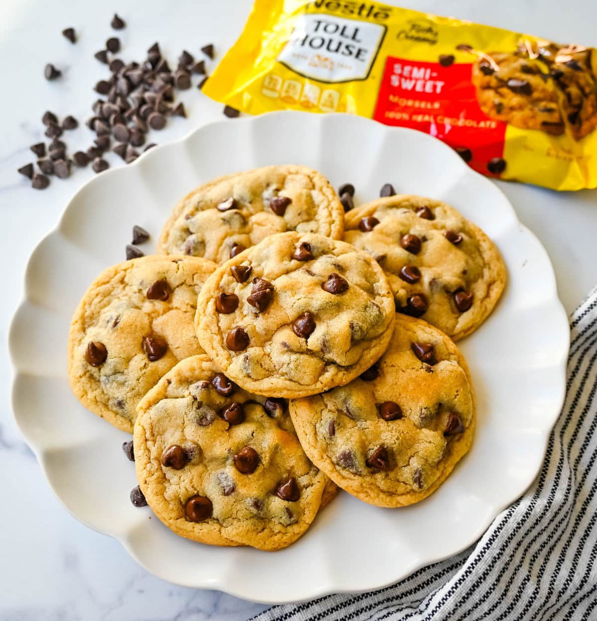 The Nestle Toll House Chocolate Chip Cookie Recipe. How to make the original Toll House chocolate chip cookie recipe on the bag. Tips for making the best Toll house chocolate chip cookies. Chocolate chip cookies on a plate with a yellow Nestle Toll House chocolate chips bag. Homemade chocolate chip cookies stacked on a plate made with Nestle toll house chocolate chips.