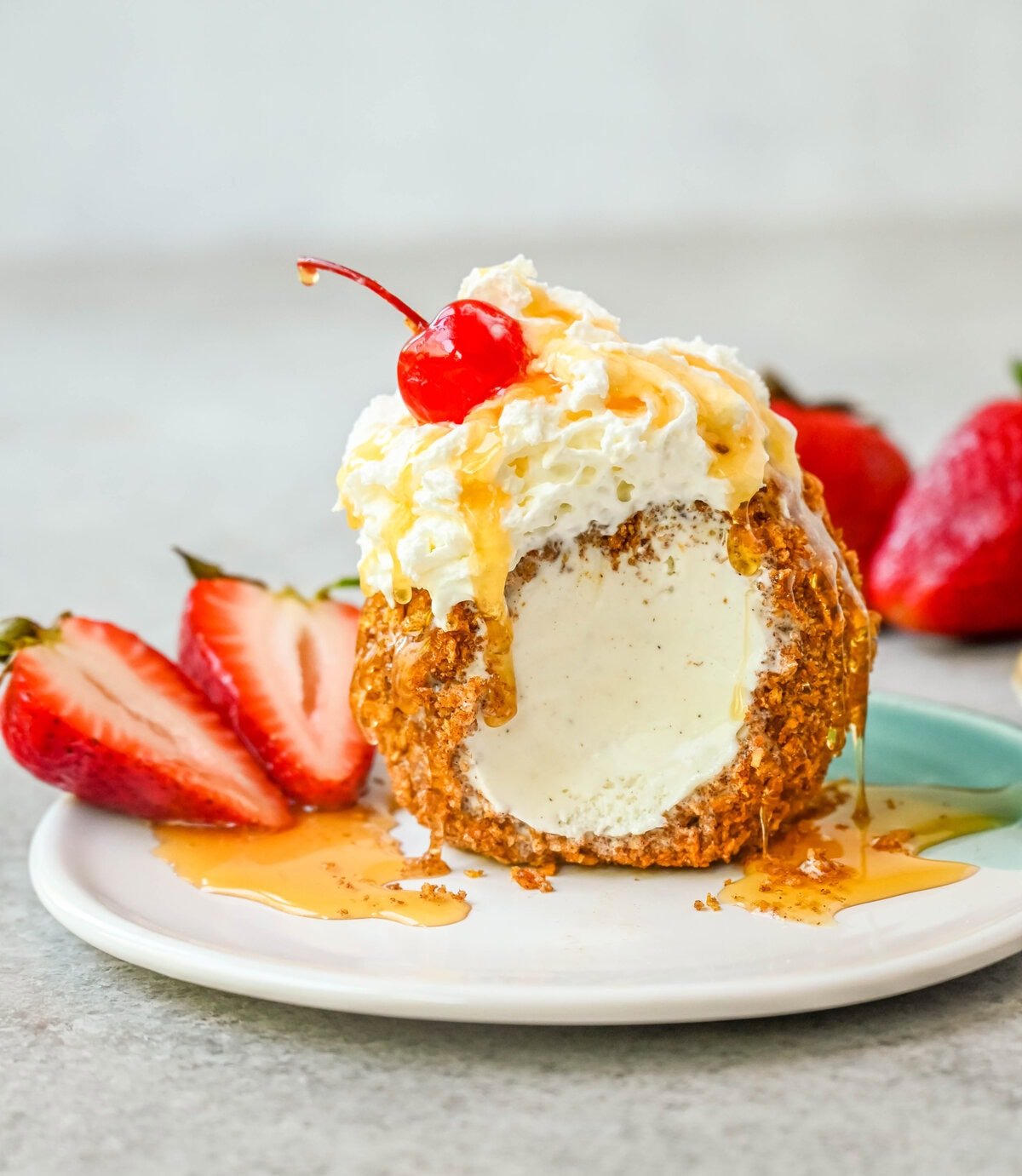 Crunchy cinnamon-sugar corn flakes coat creamy scoops of ice cream, topped with honey, whipped cream, and strawberries. This No-Fry Fried Ice Cream has zero deep-frying involved. This easy fried ice cream recipe uses corn flakes coated in buttery cinnamon sugar to mimic the crunch of a fried shell. No hot oil, no mess — just roll, freeze, and serve.