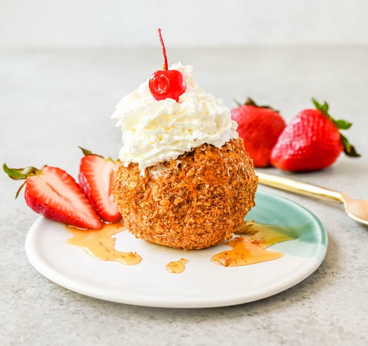 Crunchy cinnamon-sugar corn flakes coat creamy scoops of ice cream, topped with honey, whipped cream, and strawberries. This No-Fry Fried Ice Cream has zero deep-frying involved. This easy fried ice cream recipe uses corn flakes coated in buttery cinnamon sugar to mimic the crunch of a fried shell. No hot oil, no mess — just roll, freeze, and serve.