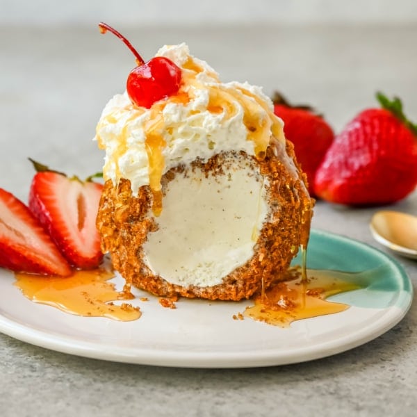 Crunchy cinnamon-sugar corn flakes coat creamy scoops of ice cream, topped with honey, whipped cream, and strawberries. This No-Fry Fried Ice Cream has zero deep-frying involved. This easy fried ice cream recipe uses corn flakes coated in buttery cinnamon sugar to mimic the crunch of a fried shell. No hot oil, no mess — just roll, freeze, and serve.