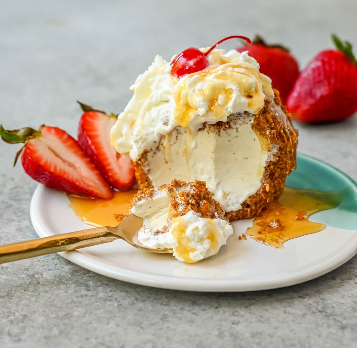 Crunchy cinnamon-sugar corn flakes coat creamy scoops of ice cream, topped with honey, whipped cream, and strawberries. This No-Fry Fried Ice Cream has zero deep-frying involved. This easy fried ice cream recipe uses corn flakes coated in buttery cinnamon sugar to mimic the crunch of a fried shell. No hot oil, no mess — just roll, freeze, and serve.