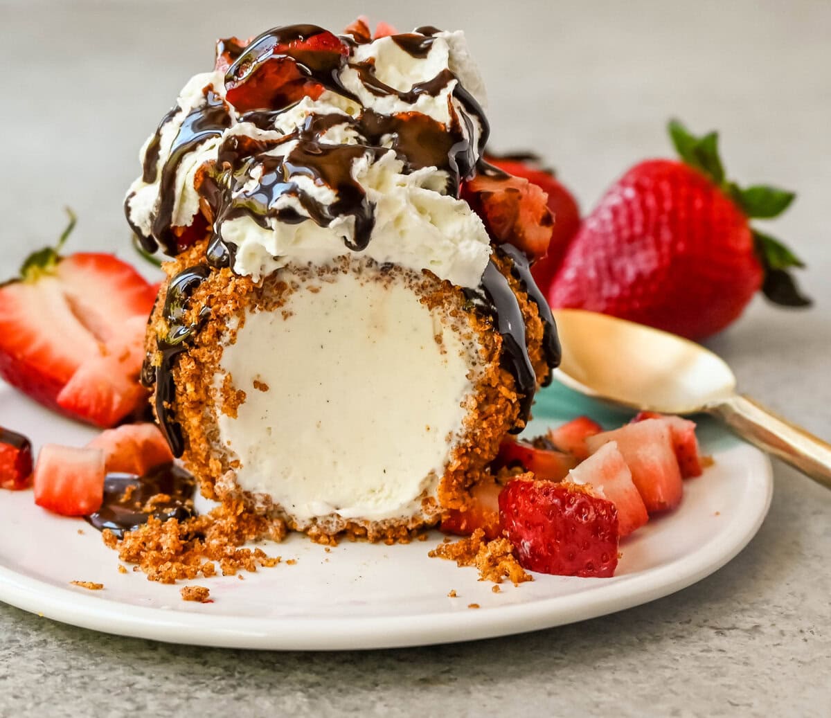 Crunchy cinnamon-sugar corn flakes coat creamy scoops of ice cream, topped with honey, whipped cream, and strawberries. This No-Fry Fried Ice Cream has zero deep-frying involved. This easy fried ice cream recipe uses corn flakes coated in buttery cinnamon sugar to mimic the crunch of a fried shell. No hot oil, no mess — just roll, freeze, and serve.