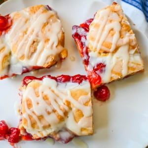 If you're craving cherry pie but want an easier recipe, these Cherry Pie Bars with a Cookie Crust are the answer. With a soft, buttery crust on the bottom, a layer of sweet cherry pie filling, and golden cookie crumbles on top, and a drizzle of icing. These may be even better than cherry pie without all of the work.