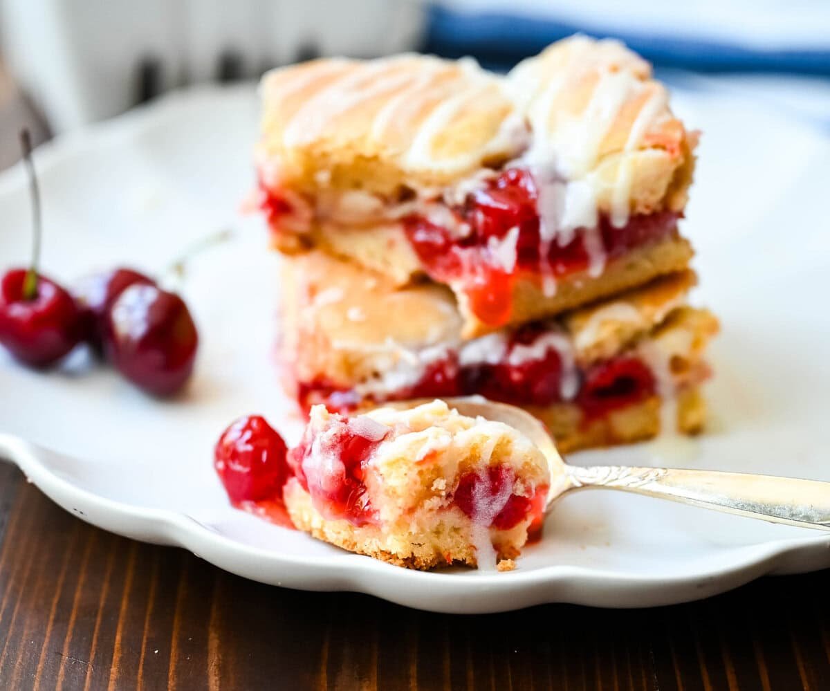 If you're craving cherry pie but want an easier recipe, these Cherry Pie Bars with a Cookie Crust are the answer. With a soft, buttery crust on the bottom, a layer of sweet cherry pie filling, and golden cookie crumbles on top, and a drizzle of icing. These may be even better than cherry pie without all of the work.