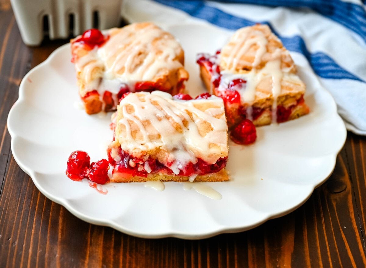If you're craving cherry pie but want an easier recipe, these Cherry Pie Bars with a Cookie Crust are the answer. With a soft, buttery crust on the bottom, a layer of sweet cherry pie filling, and golden cookie crumbles on top, and a drizzle of icing. These may be even better than cherry pie without all of the work.