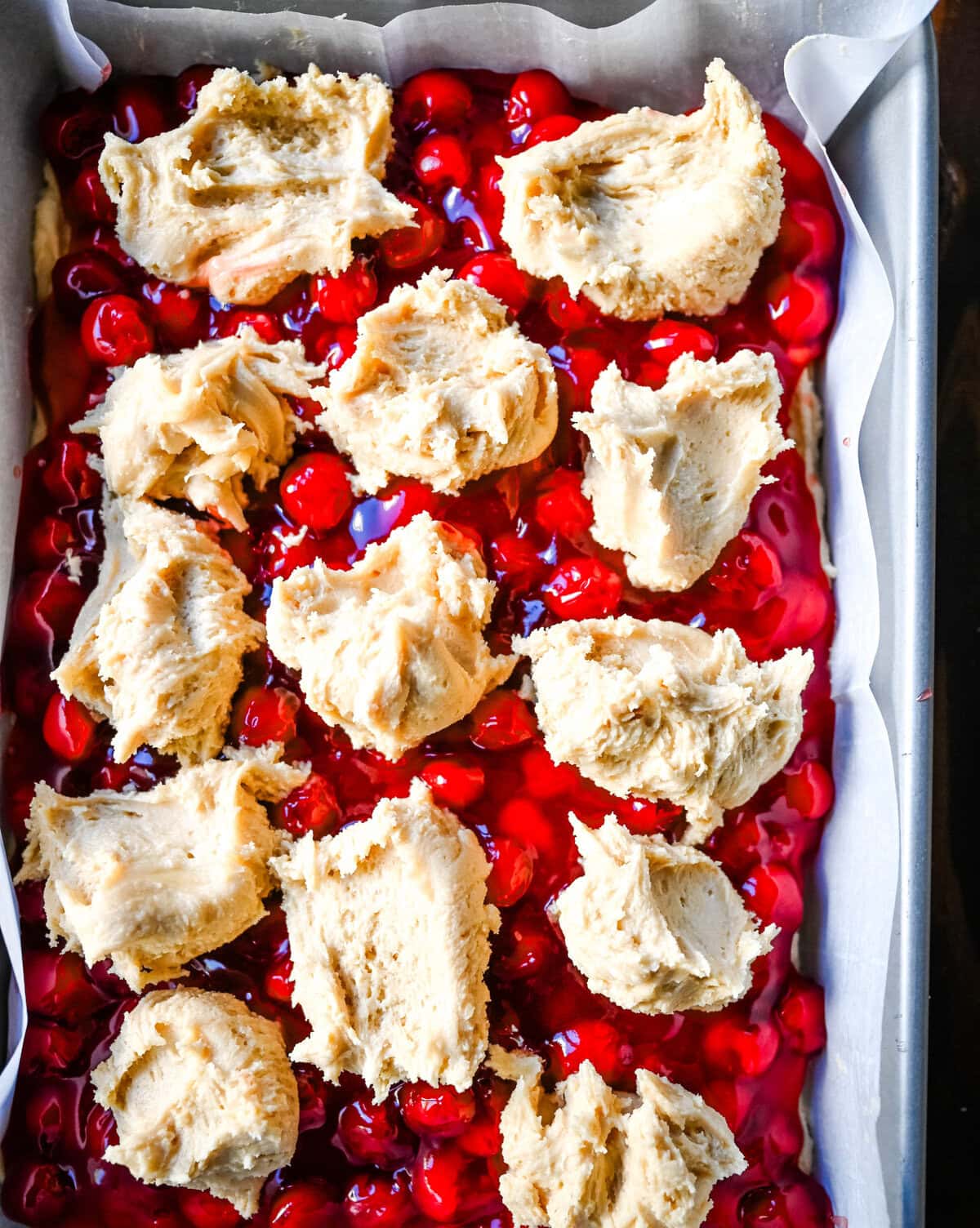 Cookie dough on top of cherry pie filling to make cherry pie cookie bars.