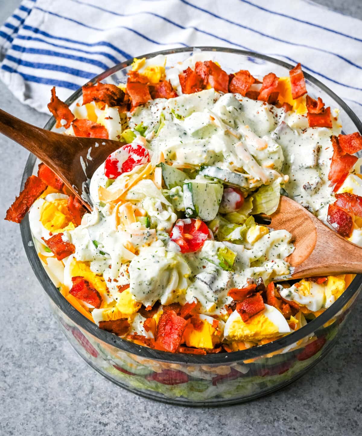 This classic Seven Layer salad is layered with iceberg lettuce, smoky bacon, hard-boiled eggs, sharp cheddar cheese, fresh veggies, and your choice of peas or garbanzo beans, plus creamy avocado. It's the ultimate make-ahead side dish, perfect for BBQs or family dinners. This easy, crowd-pleasing 7 Layer Salad is topped with a generous drizzle of homemade ranch dressing. This easy, crowd-pleasing layered salad is a beautiful, delicious side dish!