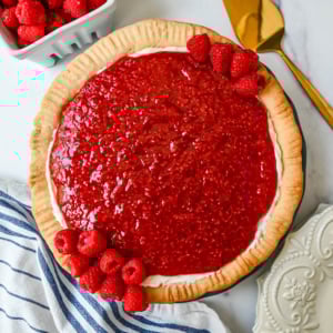 This homemade Raspberry Cream Pie is made with a sweet vanilla cream cheese cheesecake filling topped with a homemade raspberry sauce, all in a buttery, flaky homemade crust. This is a homemade take on the famous Briermere Farms raspberry cream pie and the perfect summer dessert that can be made with fresh or frozen raspberries.