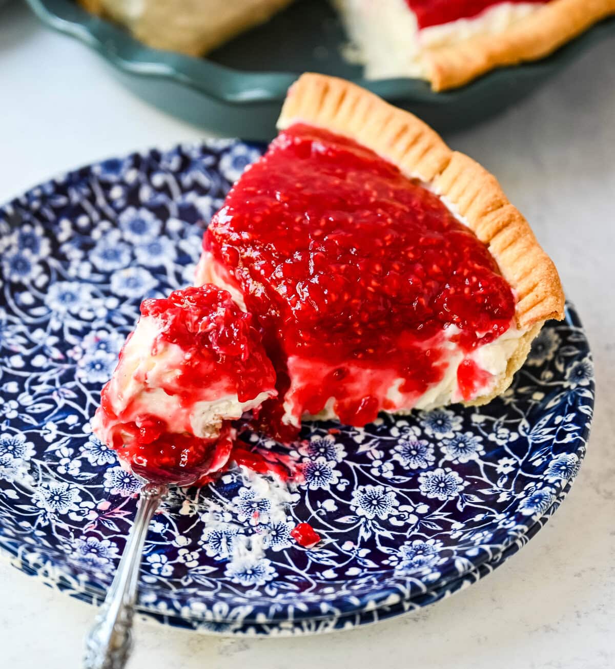 This homemade Raspberry Cream Pie is made with a sweet vanilla cream cheese cheesecake filling topped with a homemade raspberry sauce, all in a buttery, flaky homemade crust. This is a homemade take on the famous Briermere Farms raspberry cream pie and the perfect summer dessert that can be made with fresh or frozen raspberries.