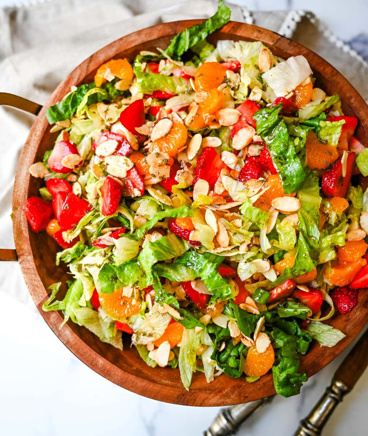 A fresh strawberry mandarin orange salad with candied almonds is the perfect summer side dish! Sweet strawberries, mandarin oranges, crunchy candied almonds, and a light homemade dressing.