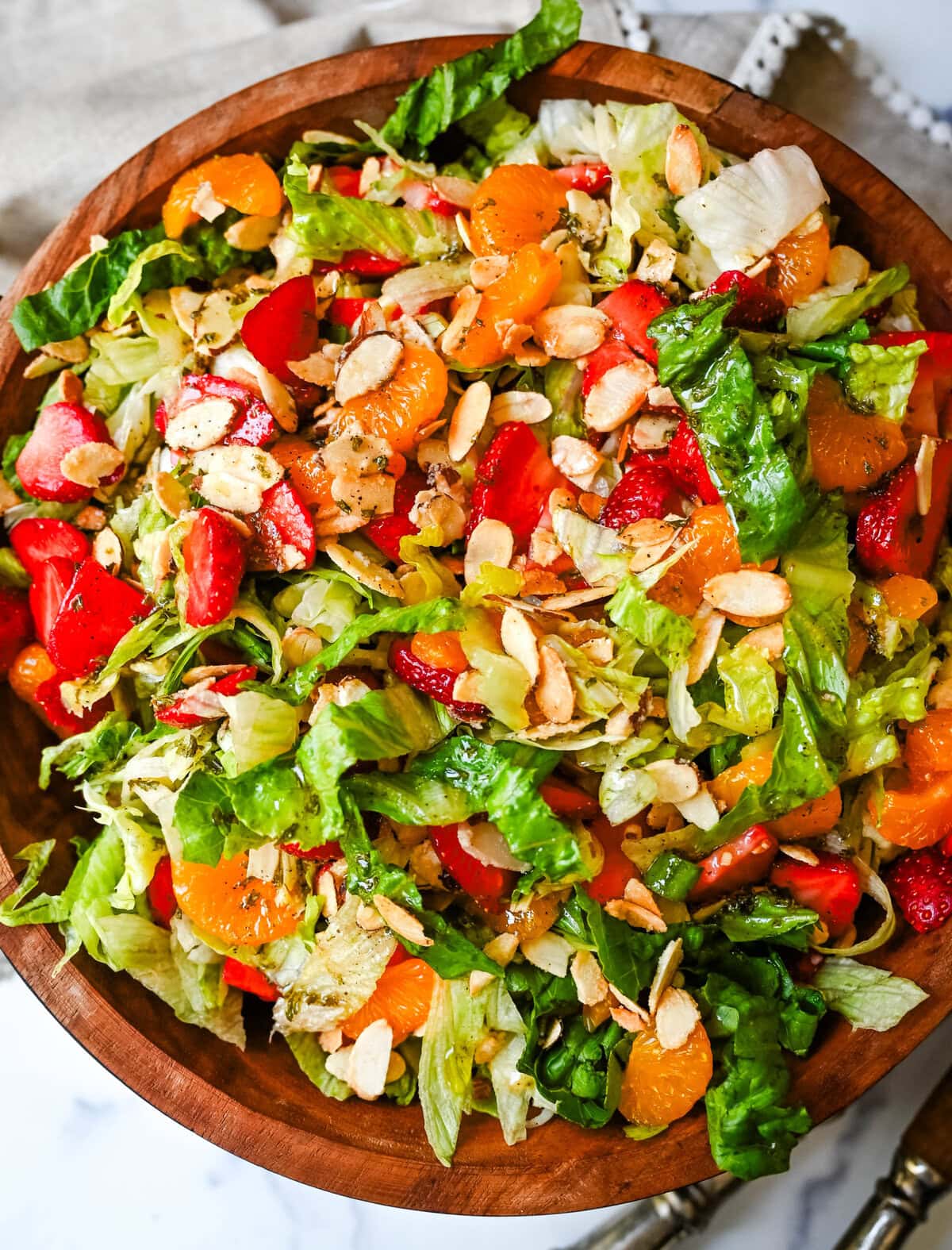 A fresh strawberry mandarin orange salad with candied almonds is the perfect summer side dish! Sweet strawberries, mandarin oranges, crunchy candied almonds, and a light homemade dressing.