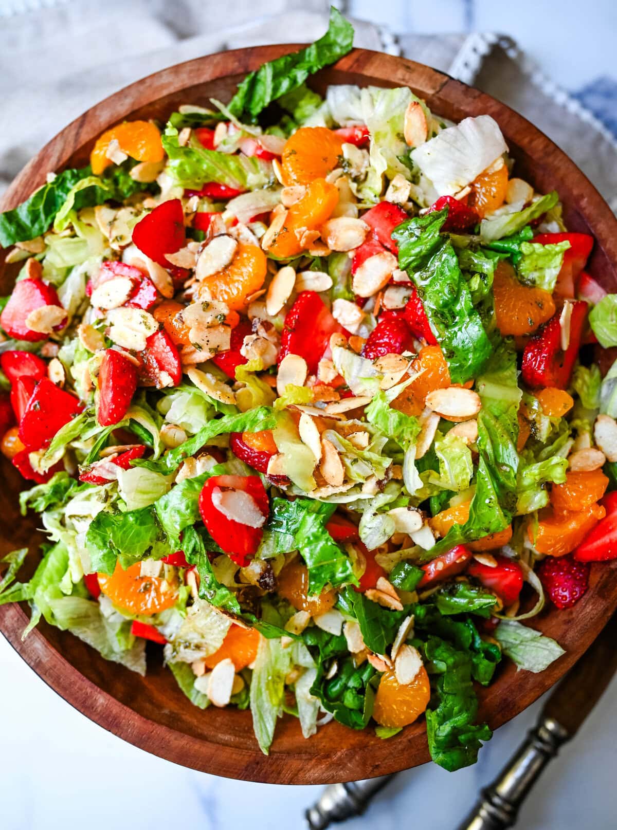 A fresh strawberry mandarin orange salad with candied almonds is the perfect summer side dish! Sweet strawberries, mandarin oranges, crunchy candied almonds, and a light homemade dressing.