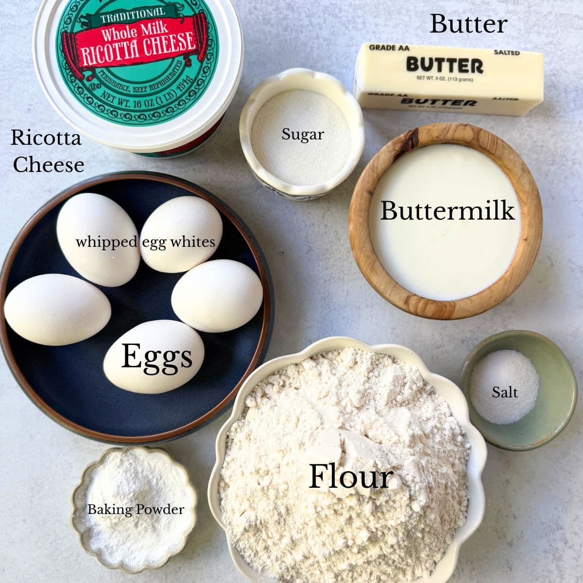 Ingredients needed to make the best fluffy pancakes including whipped egg whites, baking powder, buttermilk, and ricotta cheese.