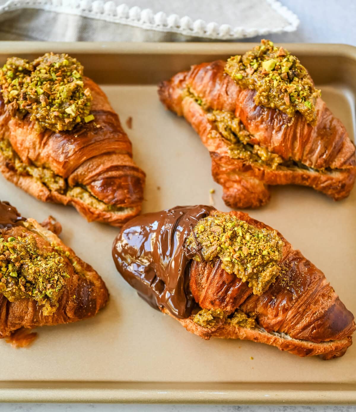 Make your own Pistachio Croissants dipped in chocolate at home in just a few easy steps! Buttery croissants are stuffed with a creamy pistachio cream filling and topped with a simple syrup and chopped pistachios for crunch. The easiest Pistachio chocolate Croissant recipe made in less than 30 minutes!