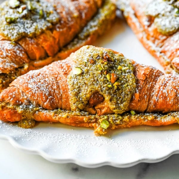 Make your own Pistachio Croissants at home in just a few easy steps! Buttery croissants are stuffed with a creamy pistachio cream filling and topped with a simple syrup and chopped pistachios for crunch. The easiest Pistachio Croissant recipe made in less than 30 minutes!