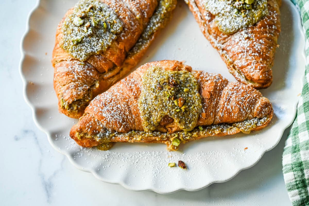 Make your own Pistachio Croissants at home in just a few easy steps! Buttery croissants are stuffed with a creamy pistachio cream filling and topped with a simple syrup and chopped pistachios for crunch. The easiest Pistachio Croissant recipe made in less than 30 minutes!